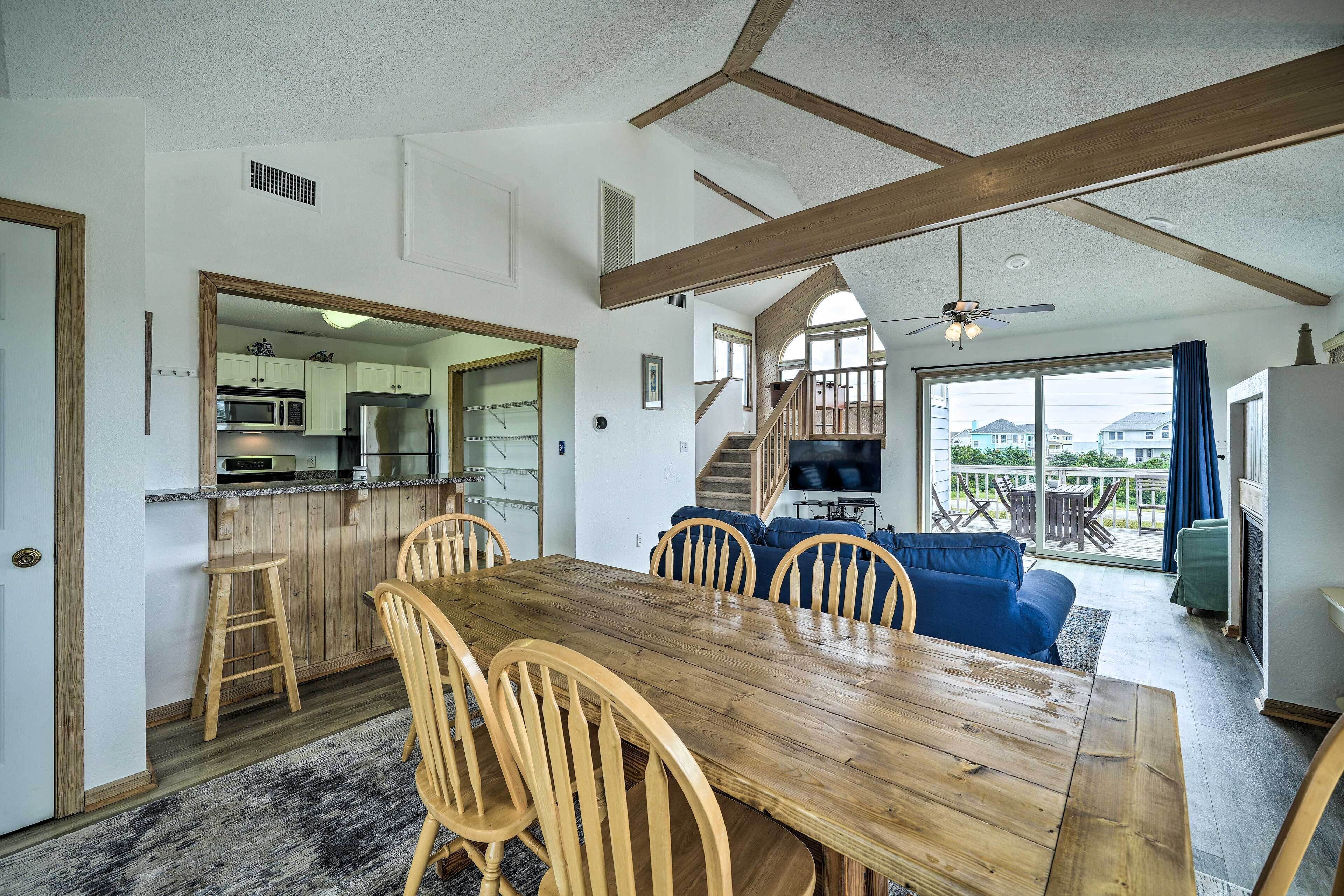Een ruime keuken met houten kastjes, een eethoek met een houten tafel en stoelen, en uitzicht op buiten door grote ramen.