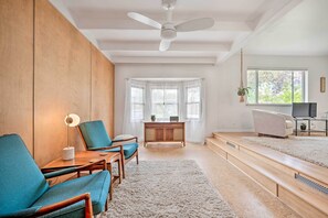 A modern living room with a wooden wall, a ceiling fan, a large window with sheer curtains, a TV stand, and a staircase leading to an upper level. - < 3 Mi to Pearl St: Home w/ Large Yard in Boulder (Boulder)