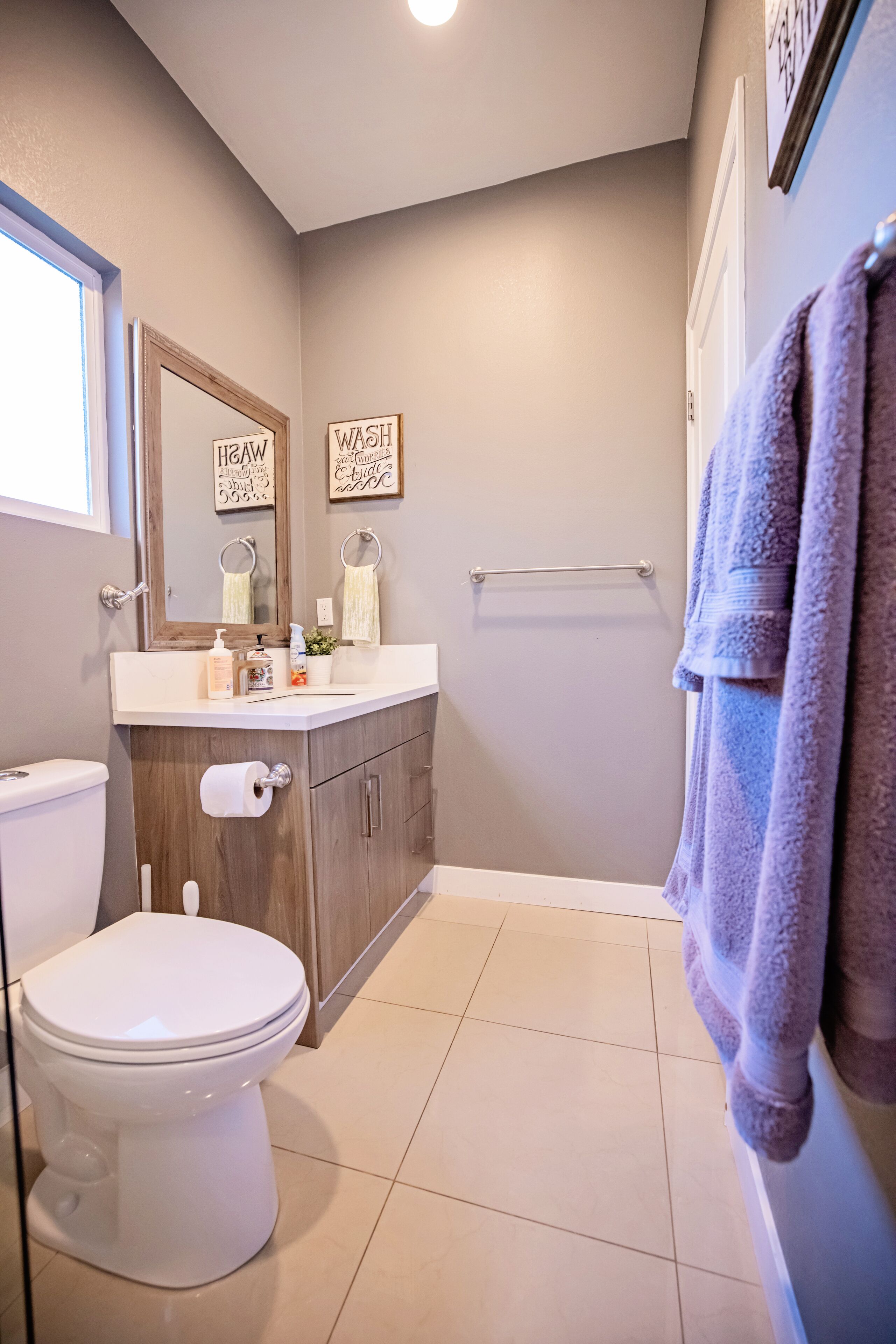 A bathroom with a toilet, sink, mirror, towel rack, and a framed sign on the wall.