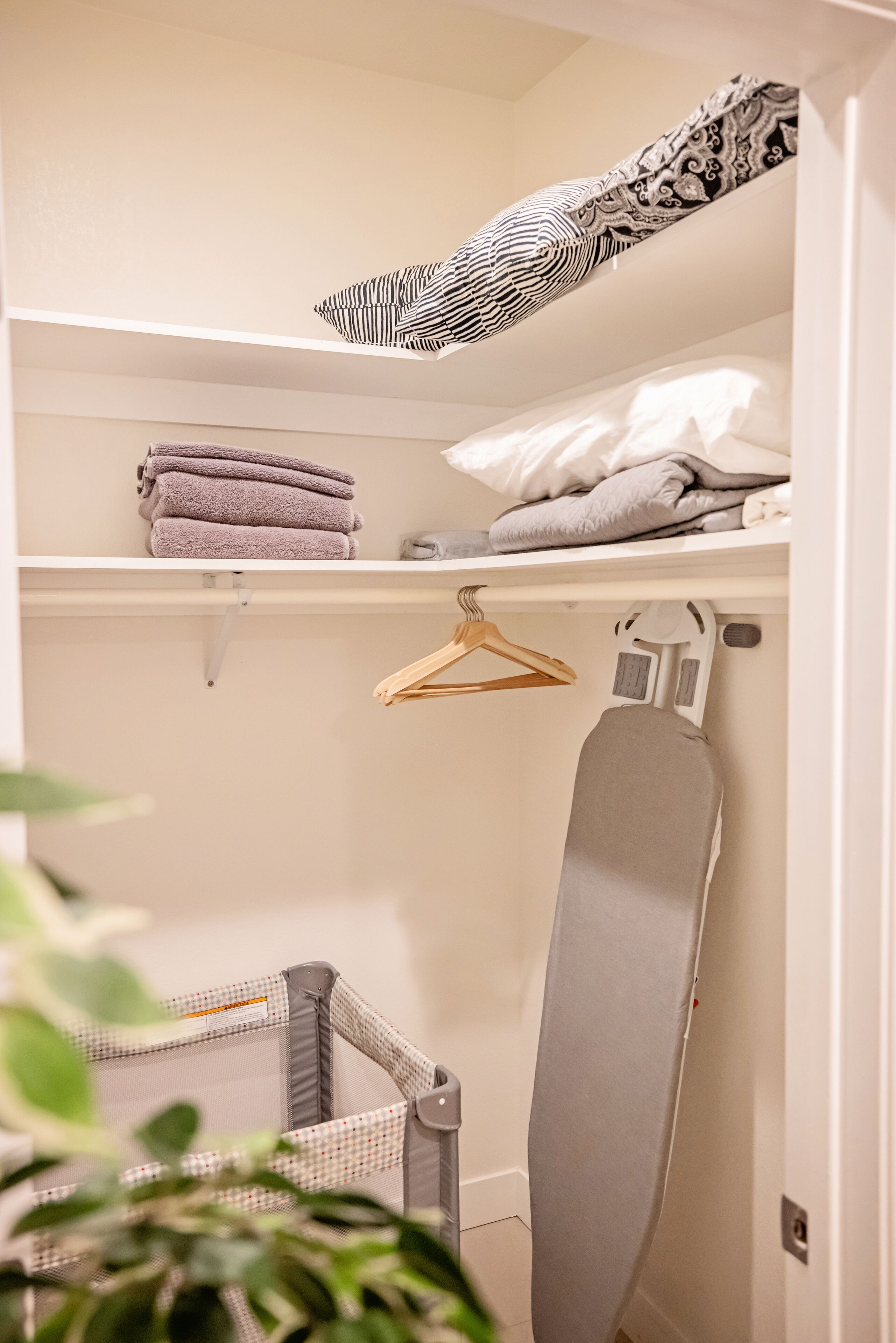 A neatly organized closet with shelves, a hanging rack, and an ironing board.