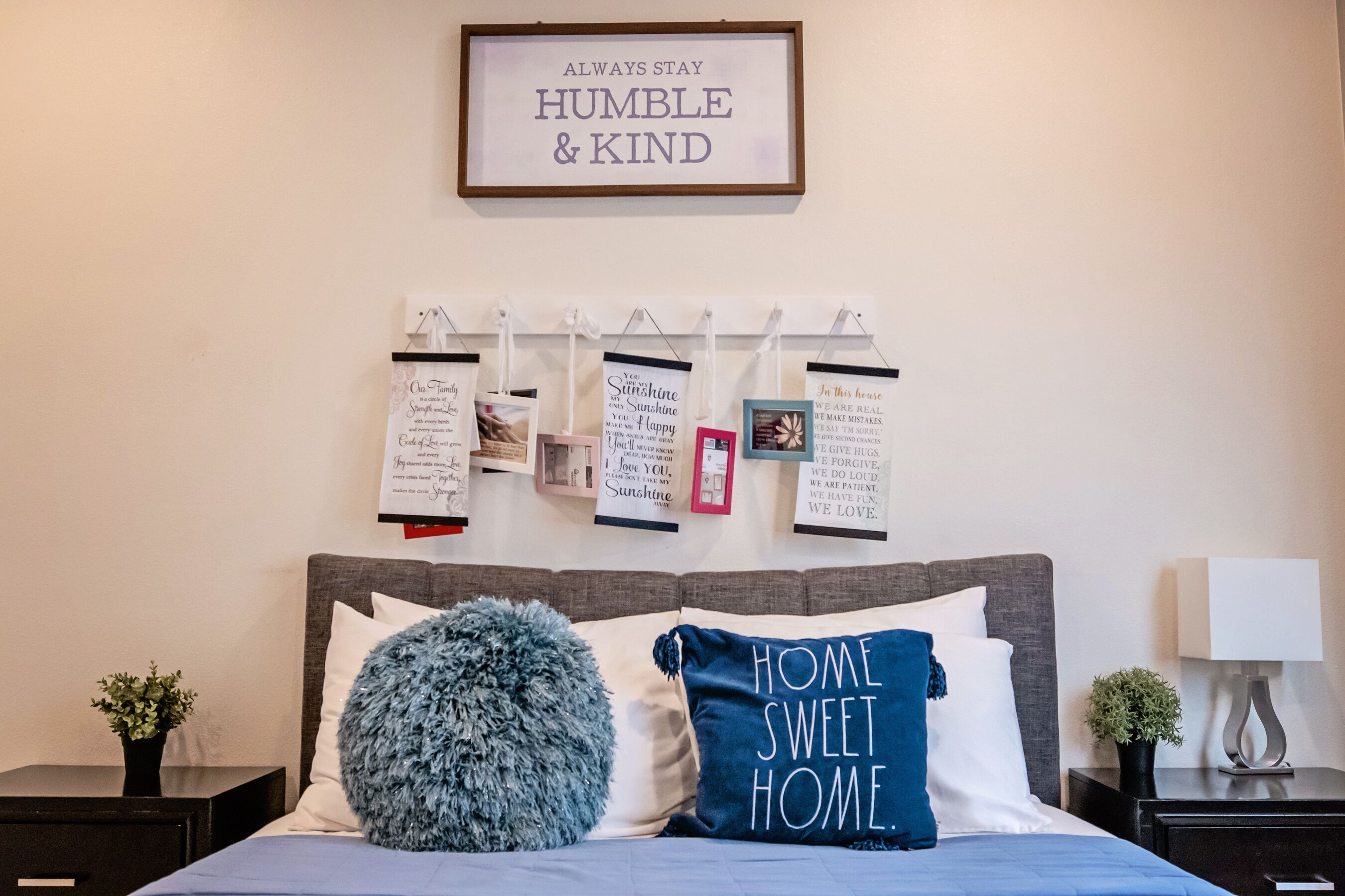 A bedroom with a bed, pillows, a wall-mounted light, and a framed inspirational quote.