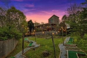 Stunning two-story home with a backyard featuring a miniature golf course and winding path surrounded by lush greenery.