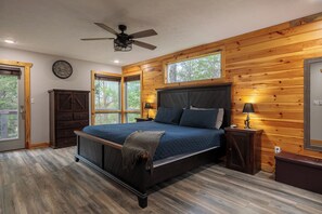 Relax in this serene bedroom with a large bed, nightstands, and a ceiling fan, offering a door to an outdoor area and expansive views.