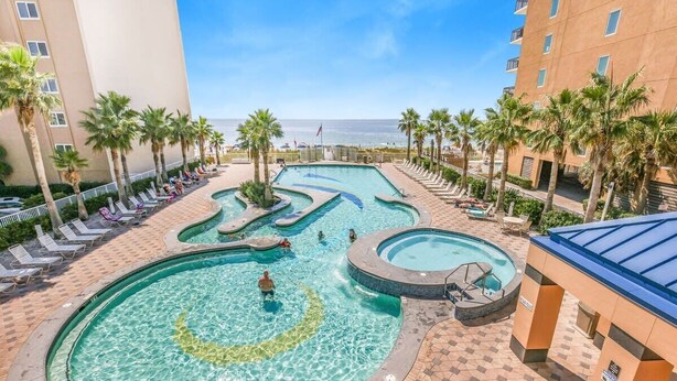 A pool area with multiple swimming pools, lounge chairs, and palm trees.