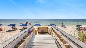A wooden boardwalk leading to a beach with umbrellas and beach chairs.