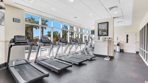 A gym with treadmills, a digital clock, and large windows with a view of palm trees.
