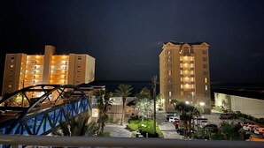 A beachfront hotel with multiple floors, a parking area, and a bridge in the foreground.