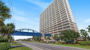 A tall hotel with multiple balconies, a pedestrian bridge, and palm trees.