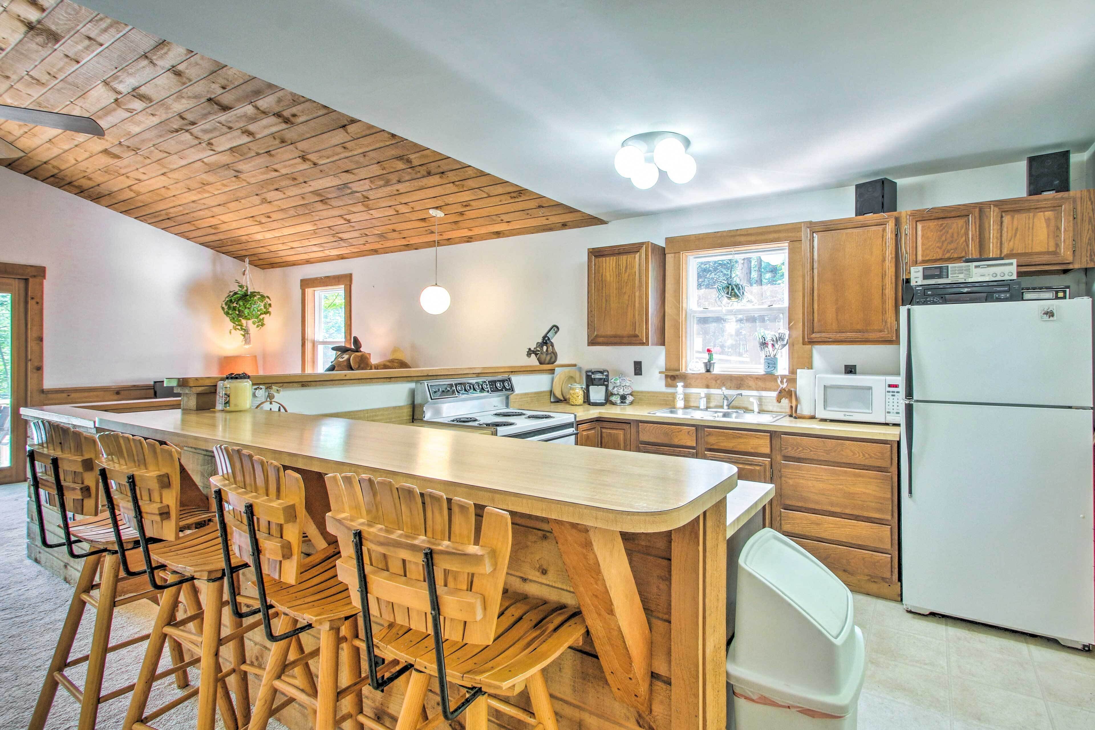 A kitchen with wooden cabinets, a central island with bar stools, a stove, microwave, and refrigerator.