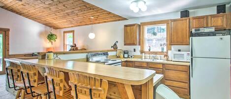 A kitchen with wooden cabinets, a central island with bar stools, a stove, microwave, and refrigerator.
