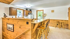 Una cocina con muebles de madera, una isla central con taburetes de bar y un reloj en la pared.