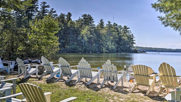 En vacker plats vid en sjö med flera Adirondack-stolar placerade på en sandstrand, med utsikt över en stilla sjö som omges av tät skog.