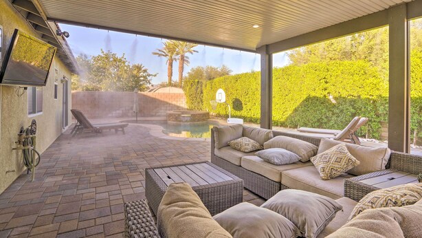 An outdoor patio with a pool, seating area, and a TV mounted on the wall. - Pool & Game Room: Pet-Friendly Indio Retreat (Indio)