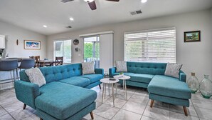 A modern living room with a sectional sofa, a ceiling fan, and a dining area with chairs and a table. - Pool & Game Room: Pet-Friendly Indio Retreat (Indio)