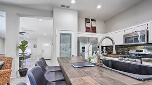 A modern kitchen with white cabinets, stainless steel appliances, a large island with seating, and a view into the dining area. - Pool & Game Room: Pet-Friendly Indio Retreat (Indio)