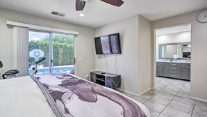 A bedroom with a large bed, a ceiling fan, a TV, and a view of the outdoors. - Pool & Game Room: Pet-Friendly Indio Retreat (Indio)