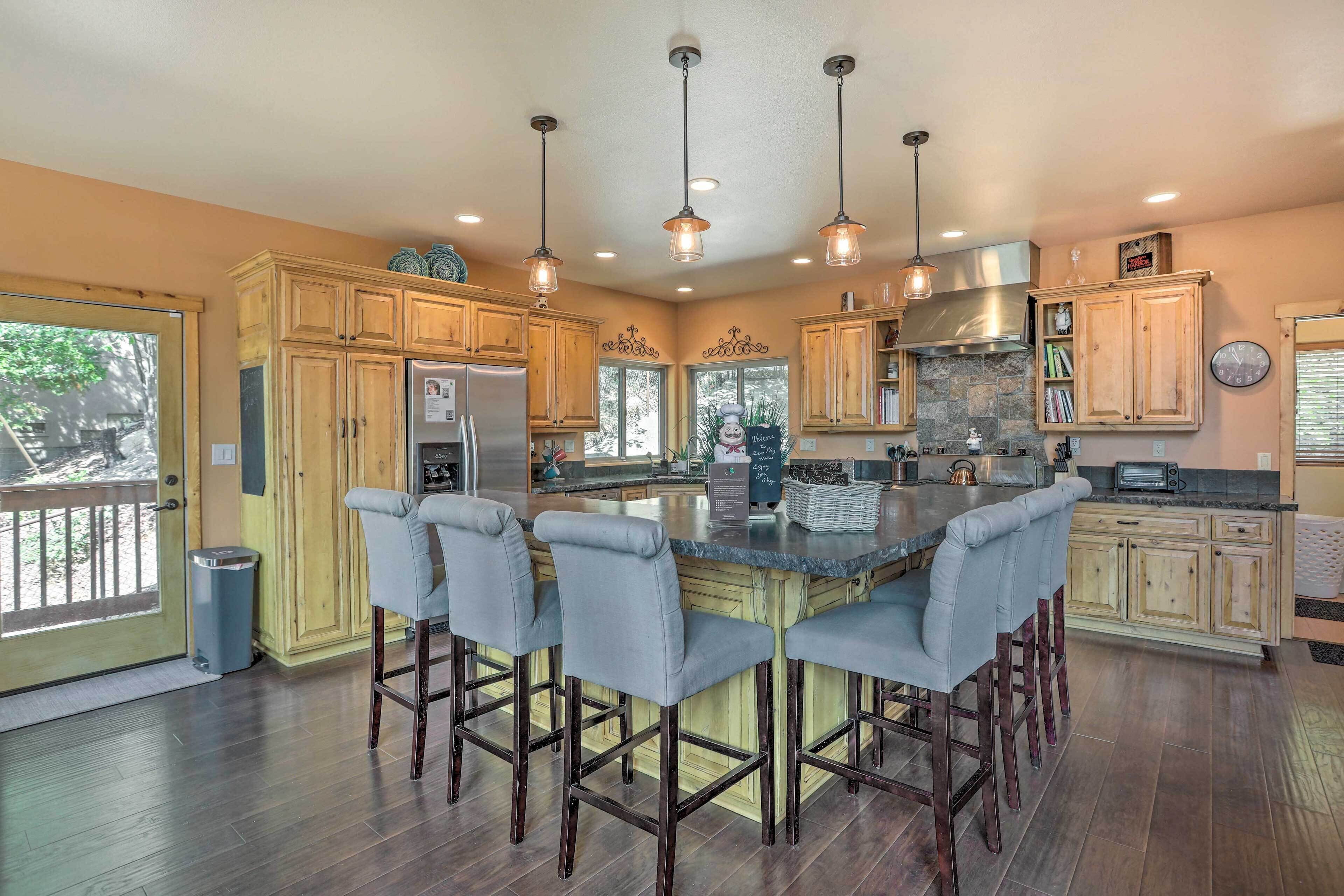 A spacious kitchen with wooden cabinets, a central island with bar stools, stainless steel appliances, and pendant lighting.