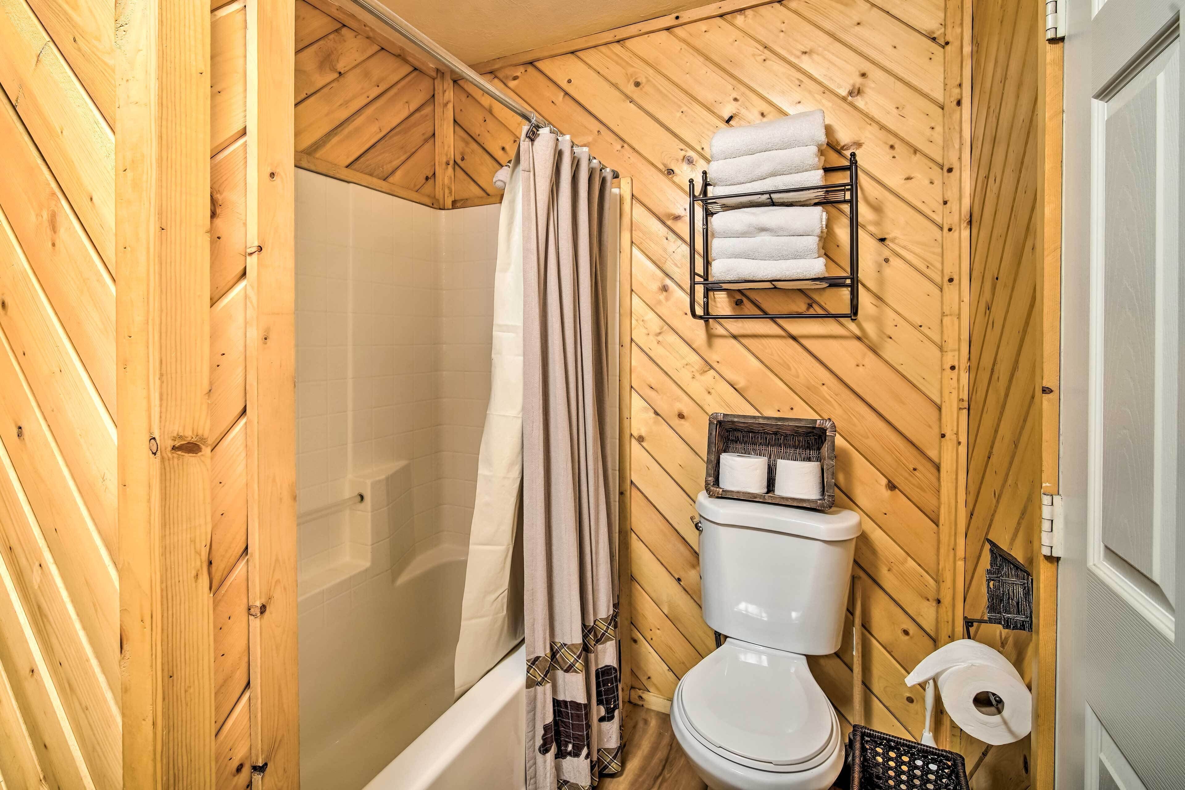 Un baño con paneles de madera, ducha, inodoro y perchero para toallas.