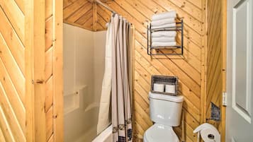 Un baño con paneles de madera, ducha, inodoro y perchero para toallas.