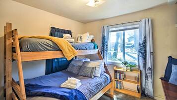 A bunk bed room with a window, a small wooden shelf with books, and a plant.