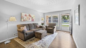 Ein Wohnzimmer mit einem Ecksofa, einem Sessel, einer Stehlampe und einem Bild an der Wand.