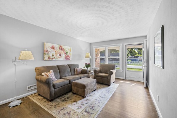 A living room with a sectional sofa, a chair, a floor lamp, and a painting on the wall.