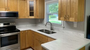 Eine Küche mit Holzschränken, einer Edelstahl-Mikrowelle, einem Backofen, einer Spüle und einem Fenster mit Jalousien.