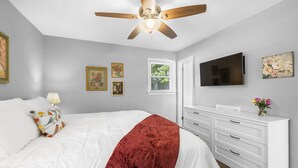 Ein Schlafzimmer mit einem Bett, einem Deckenventilator, einer Kommode, einem Fernseher und gerahmten Bildern an der Wand.