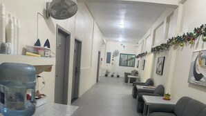 A hallway with a water dispenser, a fan, and a sofa. There are doors, a table, and a window with a view.