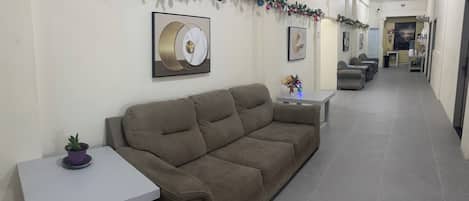 A living room with a sofa, a small table, and a potted plant. There are framed pictures on the wall and a garland with Christmas decorations.