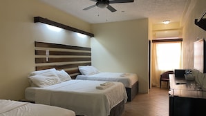 A hotel room with two beds, a ceiling fan, a desk with a chair, and a window with curtains.