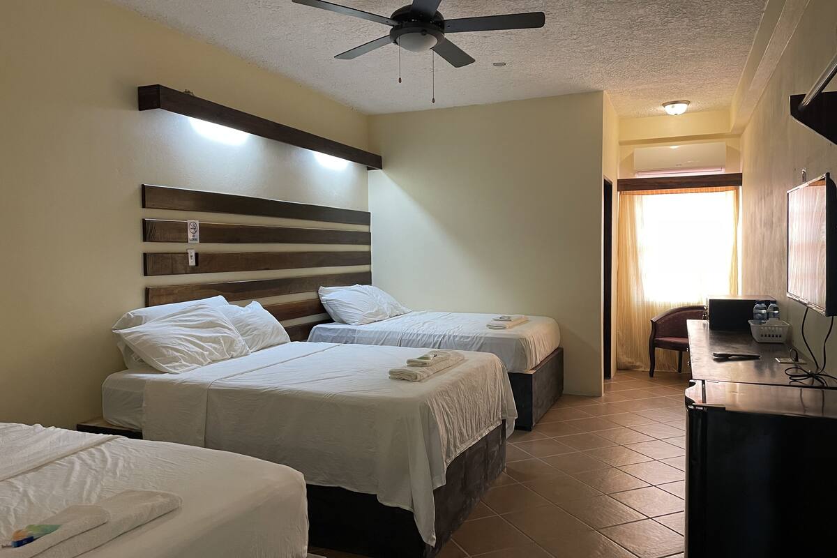 A hotel room with two beds, a ceiling fan, a desk with a chair, and a window with curtains.