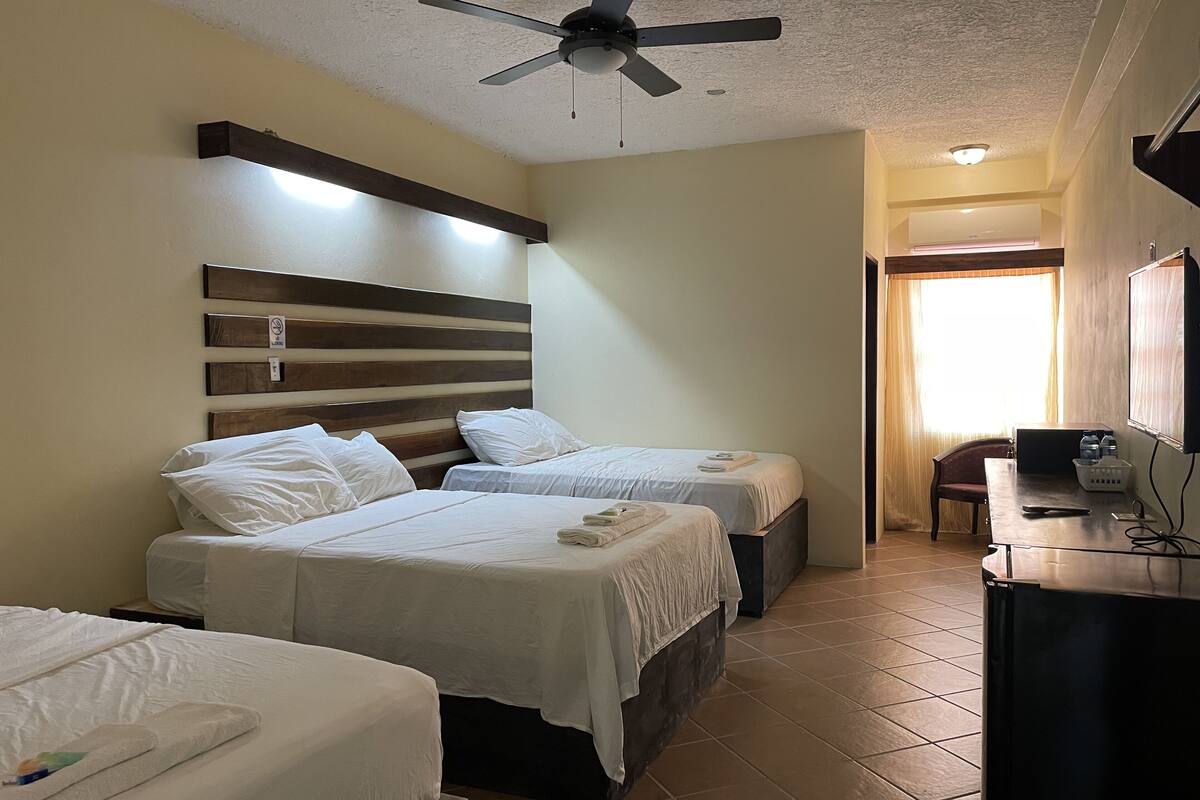 A hotel room with two beds, a ceiling fan, a desk with a chair, and a window with curtains.