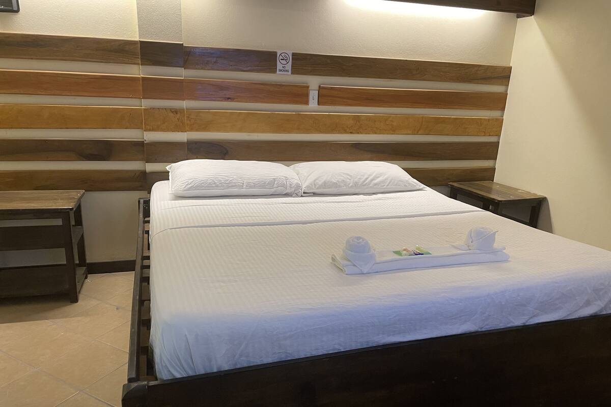 A hotel room with a wooden headboard, a bed with white linens, a small bedside table, and a nightstand.