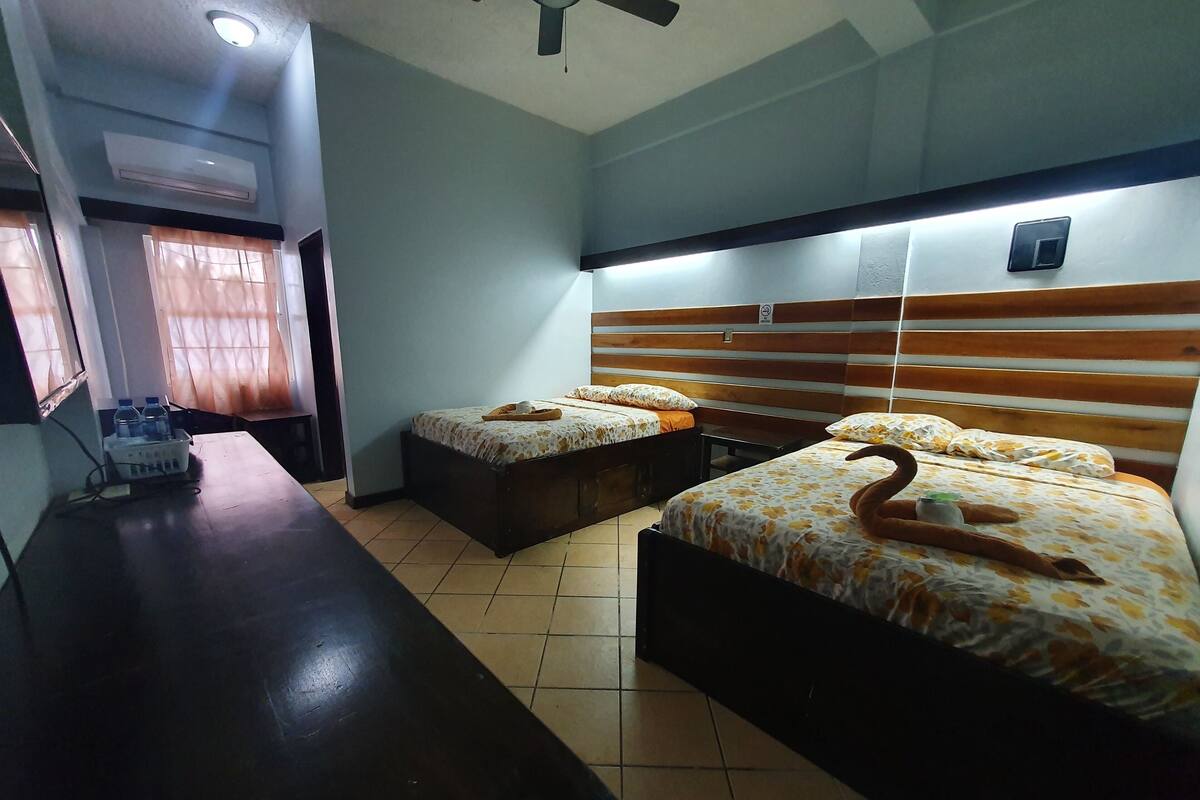 A hotel room with two beds, a desk, and an air conditioning unit.