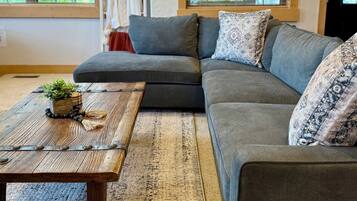 A living room with a sectional sofa, a wooden coffee table with a plant, and a patterned rug.