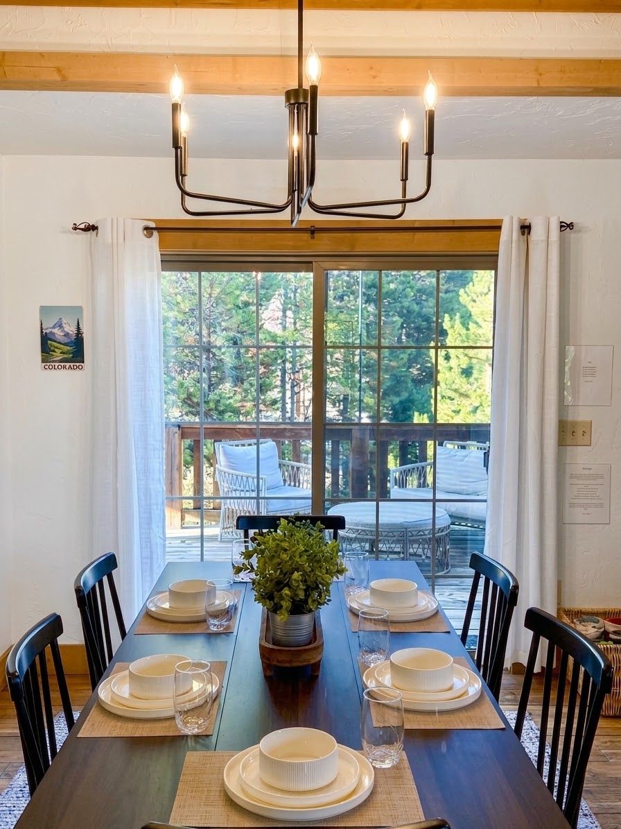 Un coin repas avec une table dressée pour six personnes, un lustre et une vue sur l’extérieur.