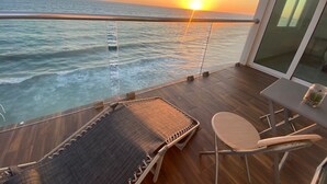 A balcony with a view of the ocean at sunset, a cushioned lounge chair, and a small table with a glass jar. - Departamento en Marina del Sol con vista al mar (Mazatlán)