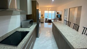 A modern kitchen with a central island, built-in appliances, and a view to the sea.