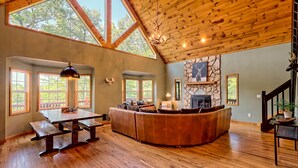 A spacious interior with a wooden ceiling, large windows, a stone fireplace, and a curved seating area. - STUNNING Mountain VIEW Lodge for 14! (Murphy)