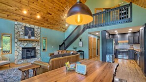 A spacious living area with a stone fireplace, a wooden ceiling, and a kitchen with dark cabinets. - STUNNING Mountain VIEW Lodge for 14! (Murphy)
