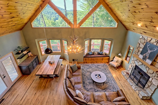 A spacious loft with a high ceiling, large windows, a stone fireplace, and a cozy seating area.
