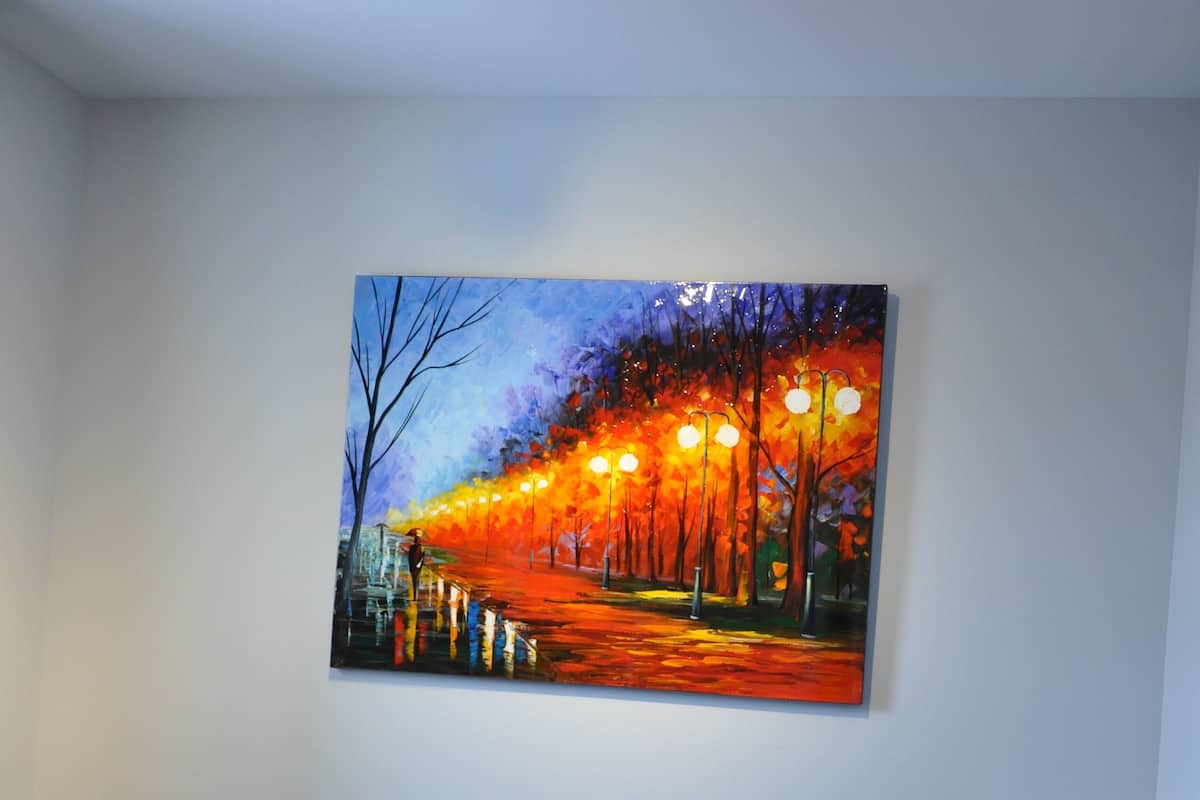 A bedroom with a bed, a painting of a city street at night, and a ceiling light.