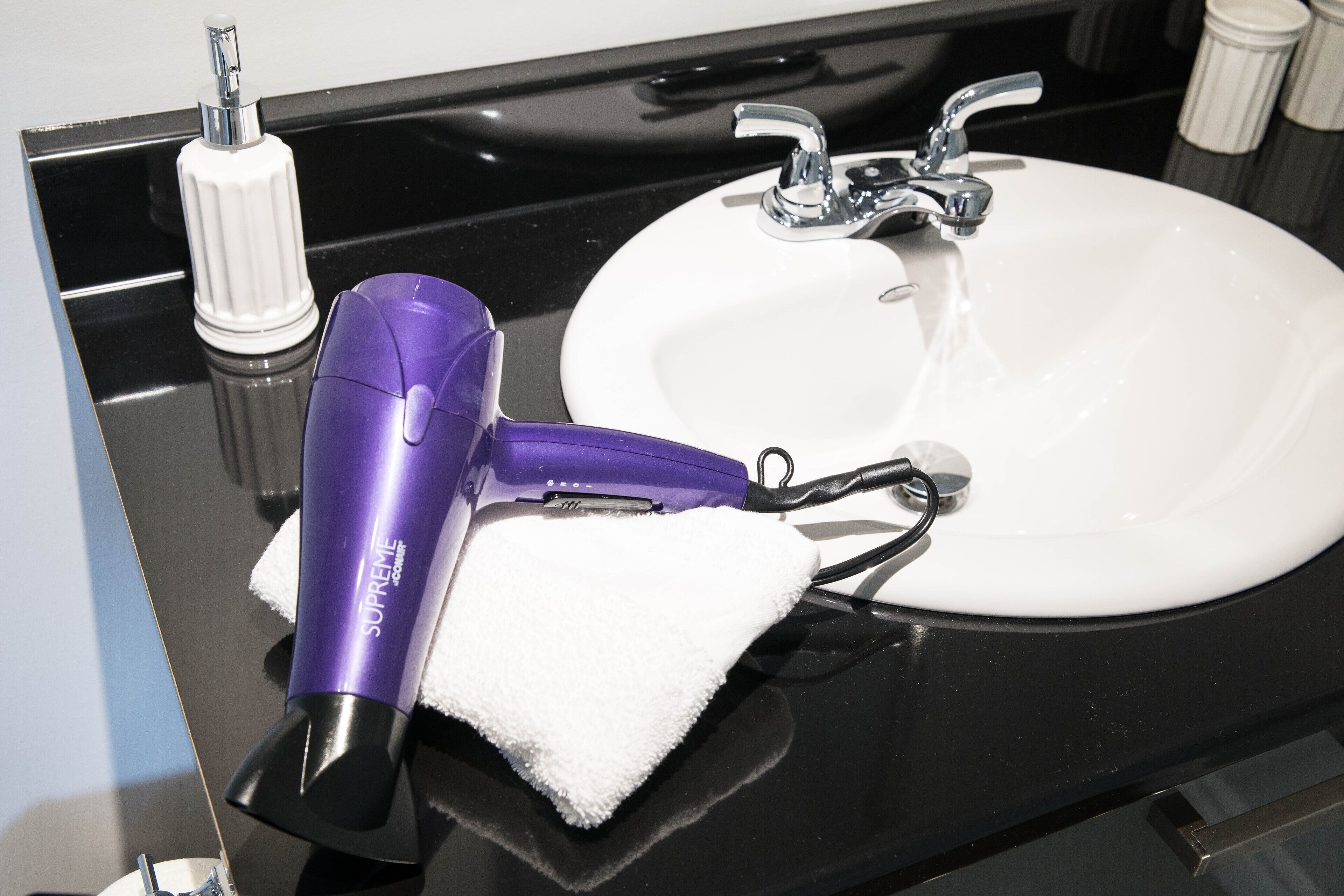 A bathroom sink with a white countertop, a purple hairdryer, and a white towel.