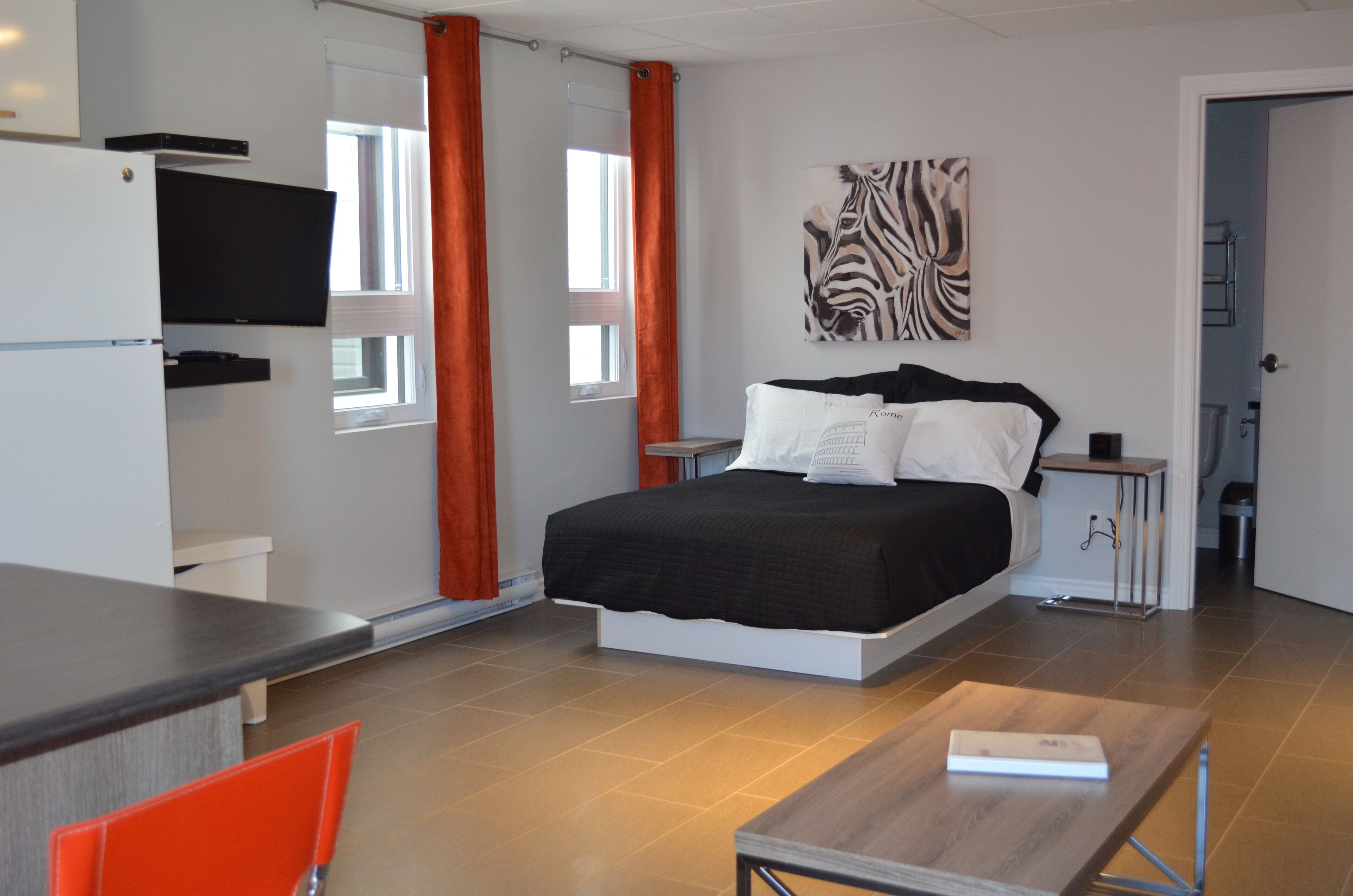 A modern bedroom with a bed, a TV mounted on the wall, and a zebra artwork.