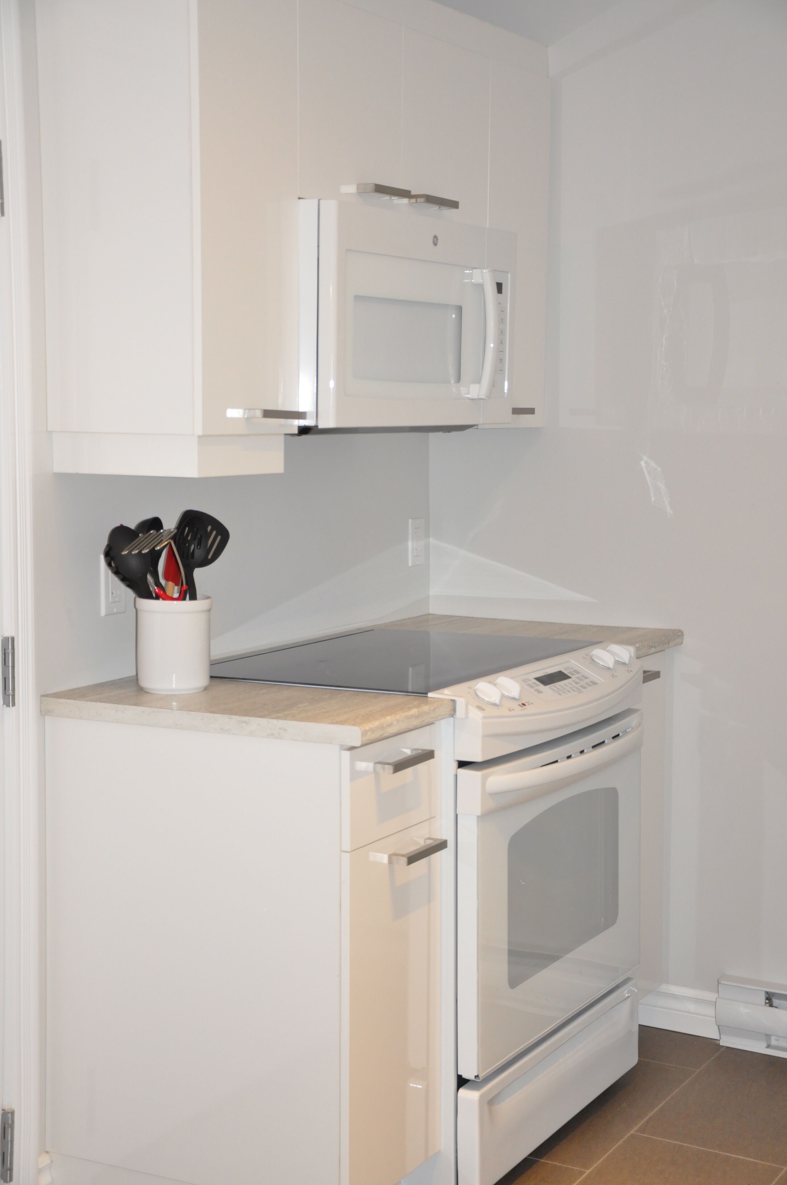 A compact kitchen with a microwave, oven, and a utensil holder on the countertop.