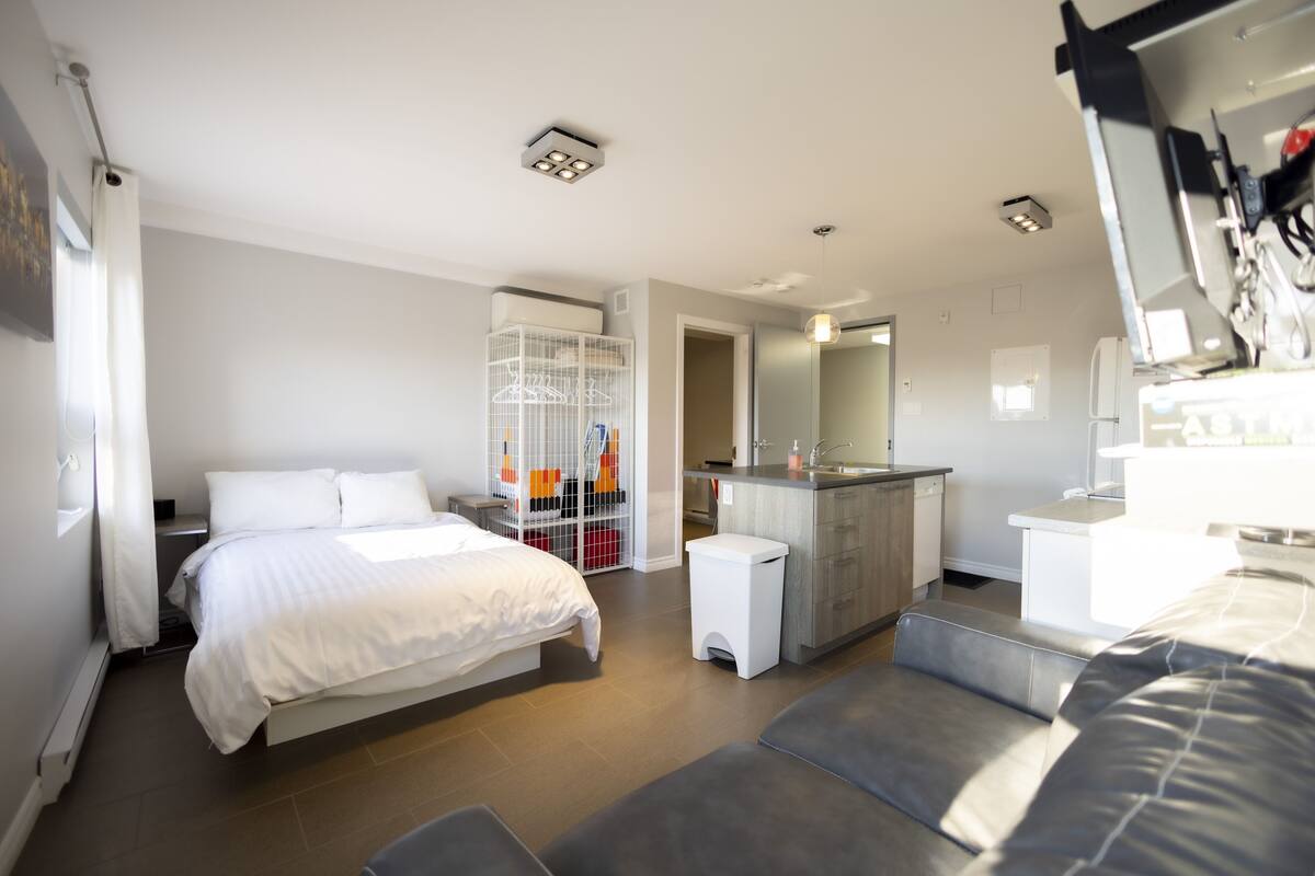 A modern hotel room with a large bed, a small bathroom, a kitchenette, and a walk-in closet.