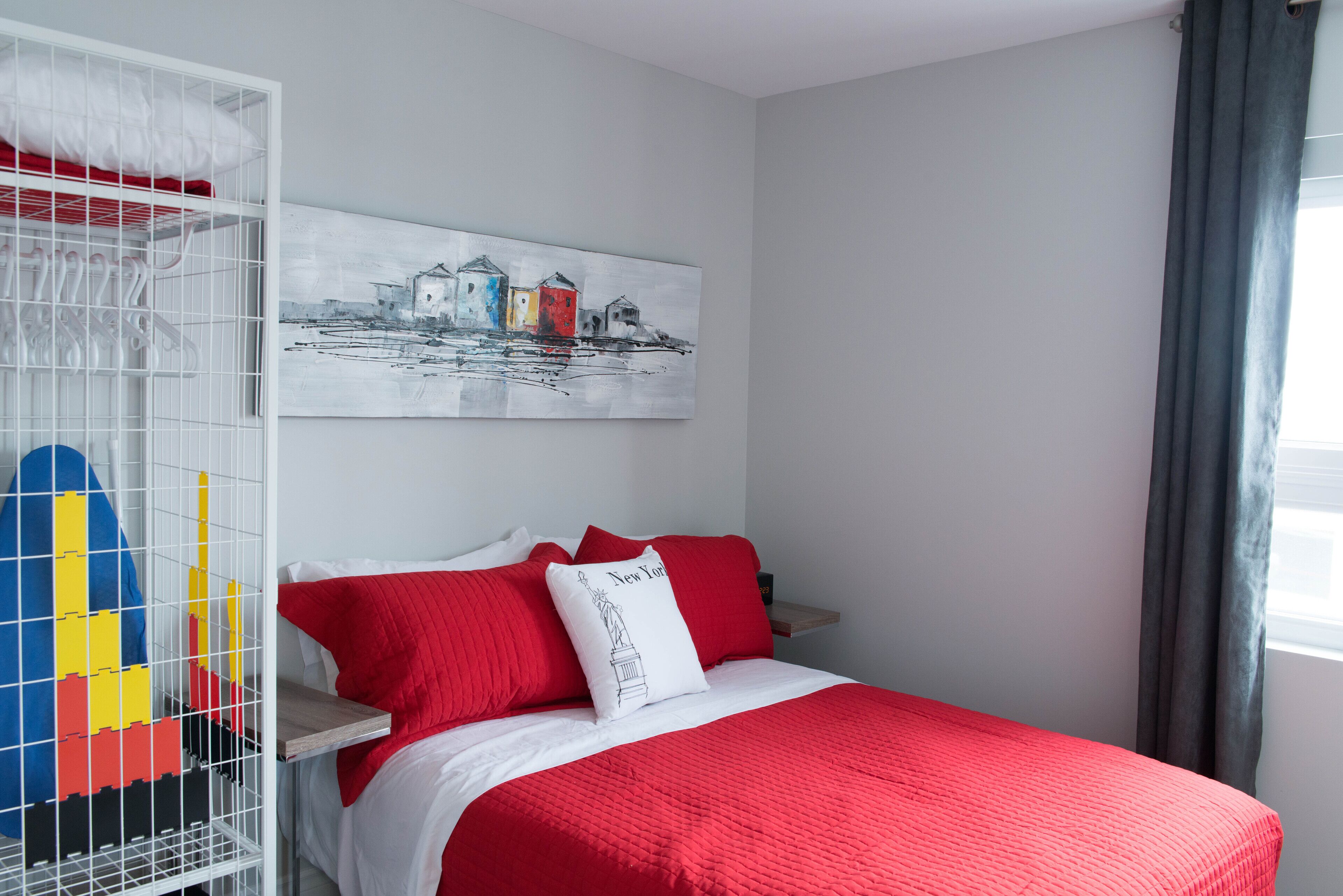 A bedroom with a bed, a white wardrobe, a painting, and a window with curtains.