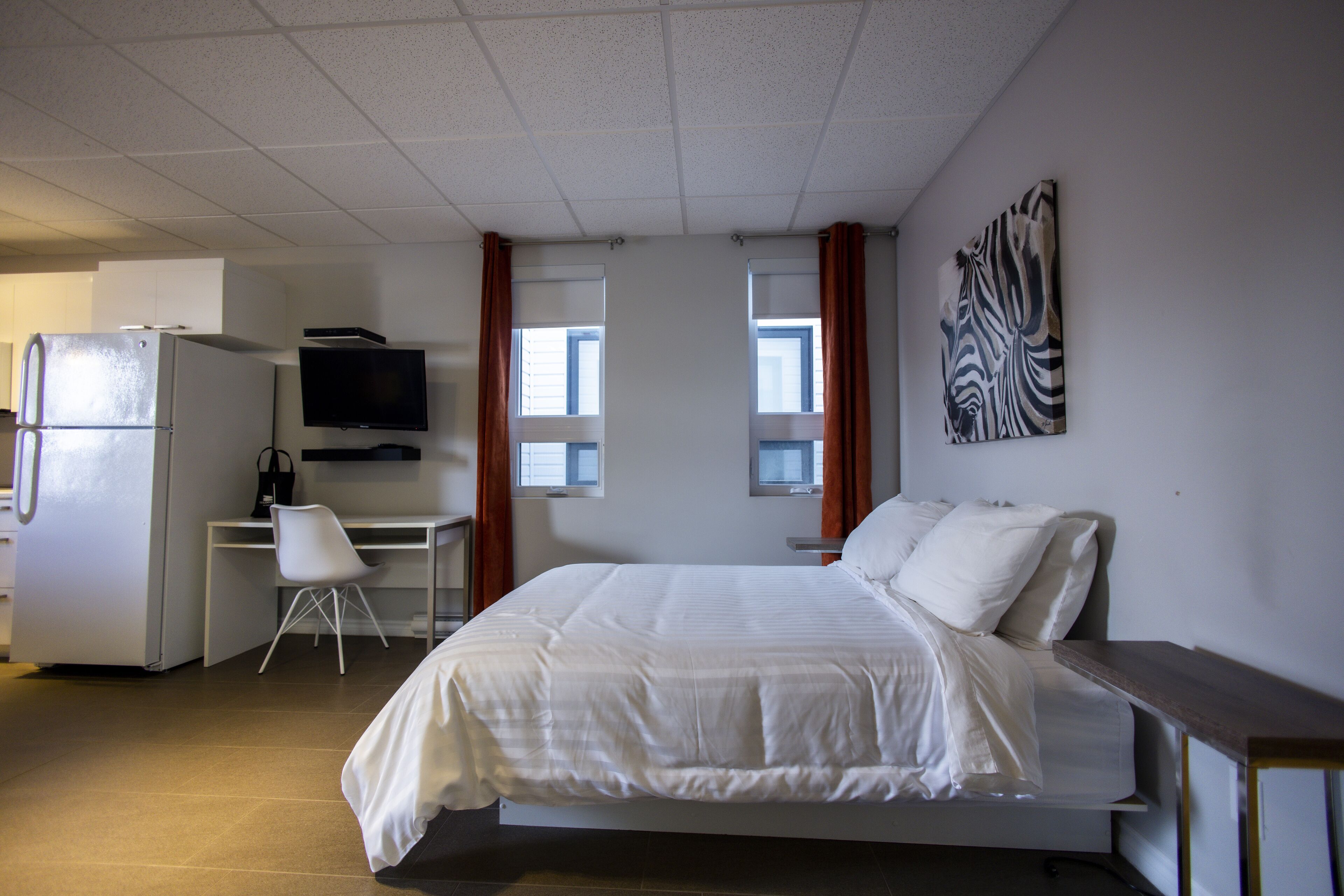 Ein Schlafzimmer mit Bett, Schreibtisch, Stuhl, Fernseher und Kühlschrank.
