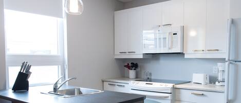 A modern kitchen with white cabinets, a built-in oven, a microwave, and a sink.